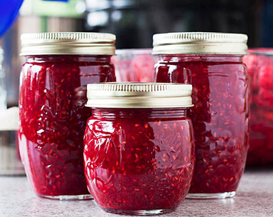 "Canning raspberry jam in an average american kitchen.  Three completed jars of jam, a bowl full of fresh rasperries, a measuring cup full f raw sugar, an empty jelly jar with a canning funnel, and pans in the background.All images in this series..."